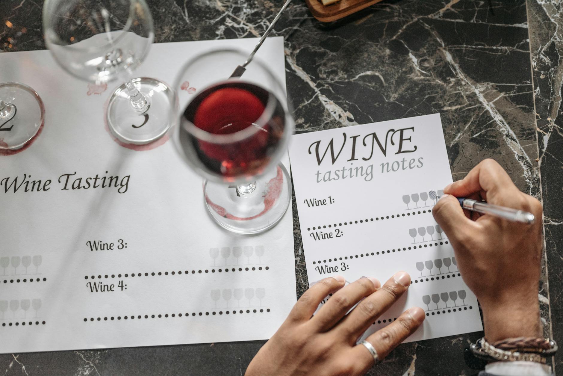 Close-up of wine tasting session with notes, glasses, and marble surface.