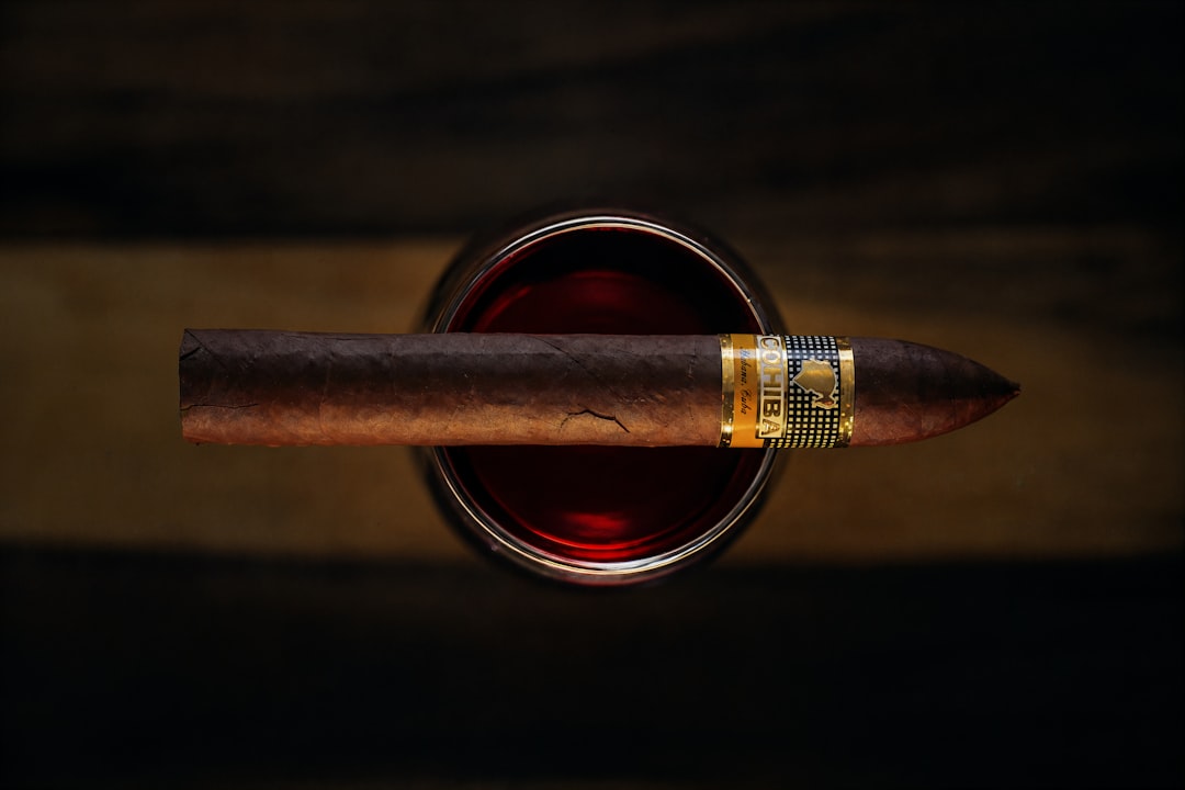 A cigar rests on a glass of dark liquid.