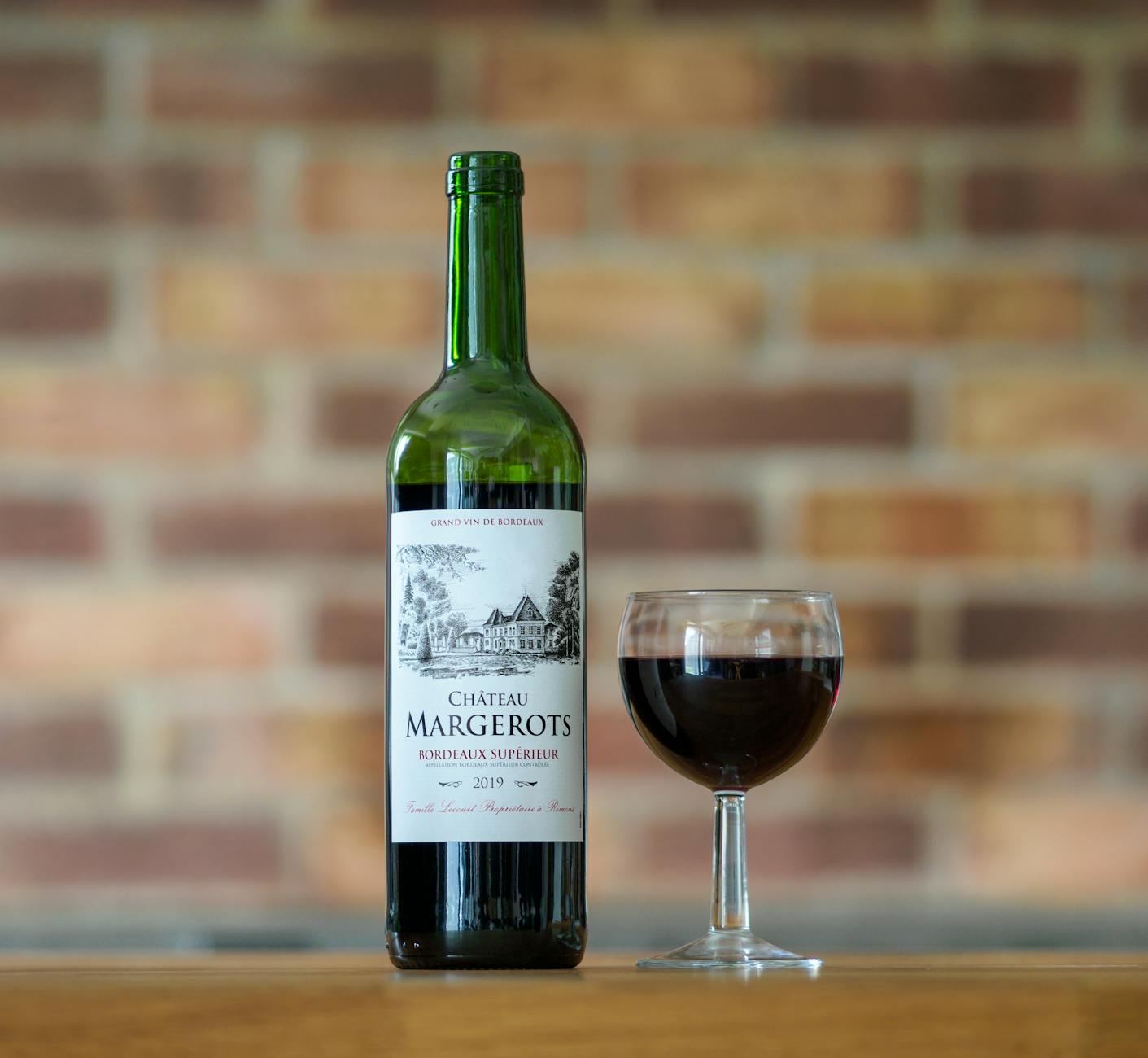 Close-up of Chateau Margerots Bordeaux wine bottle with a glass on a wooden surface.