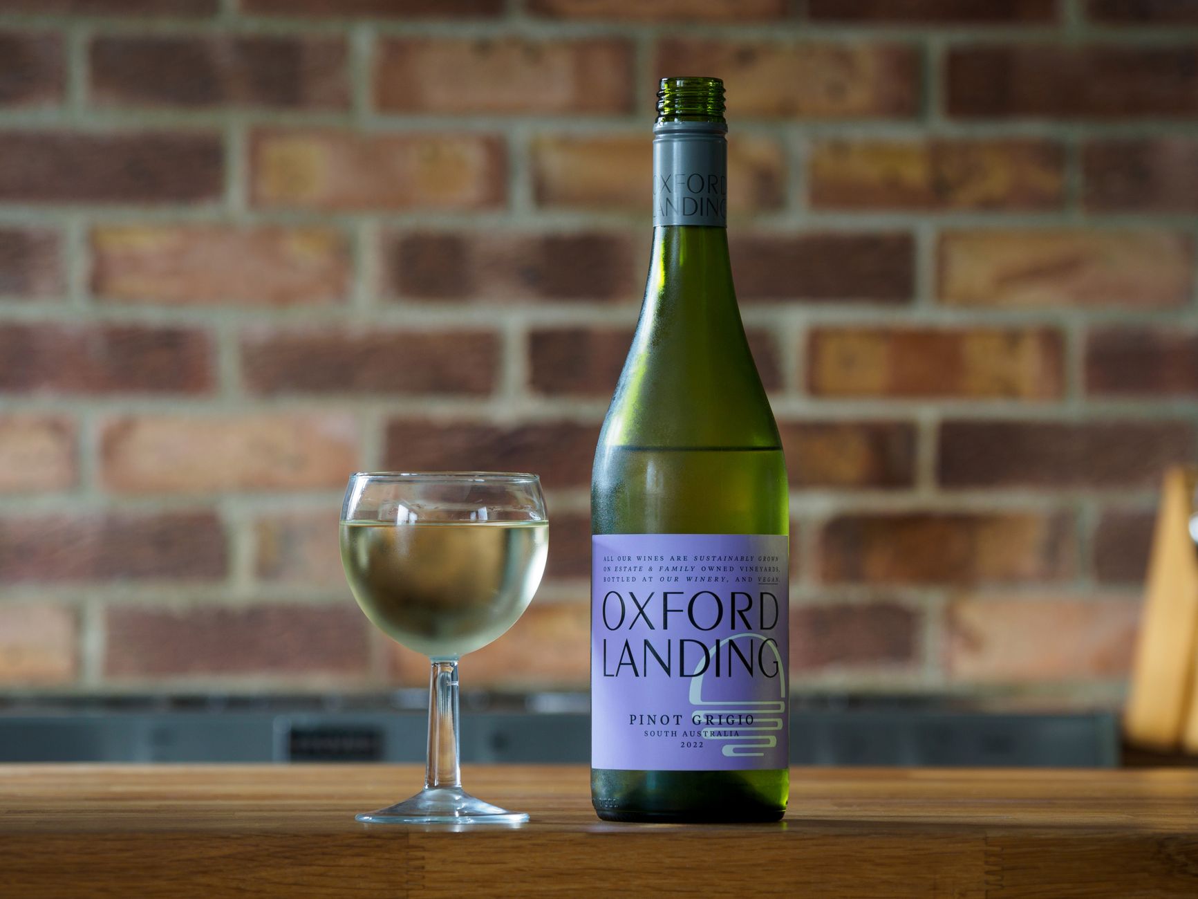 Chilled Oxford Landing Pinot Grigio against a rustic brick wall, perfect for wine enthusiasts.