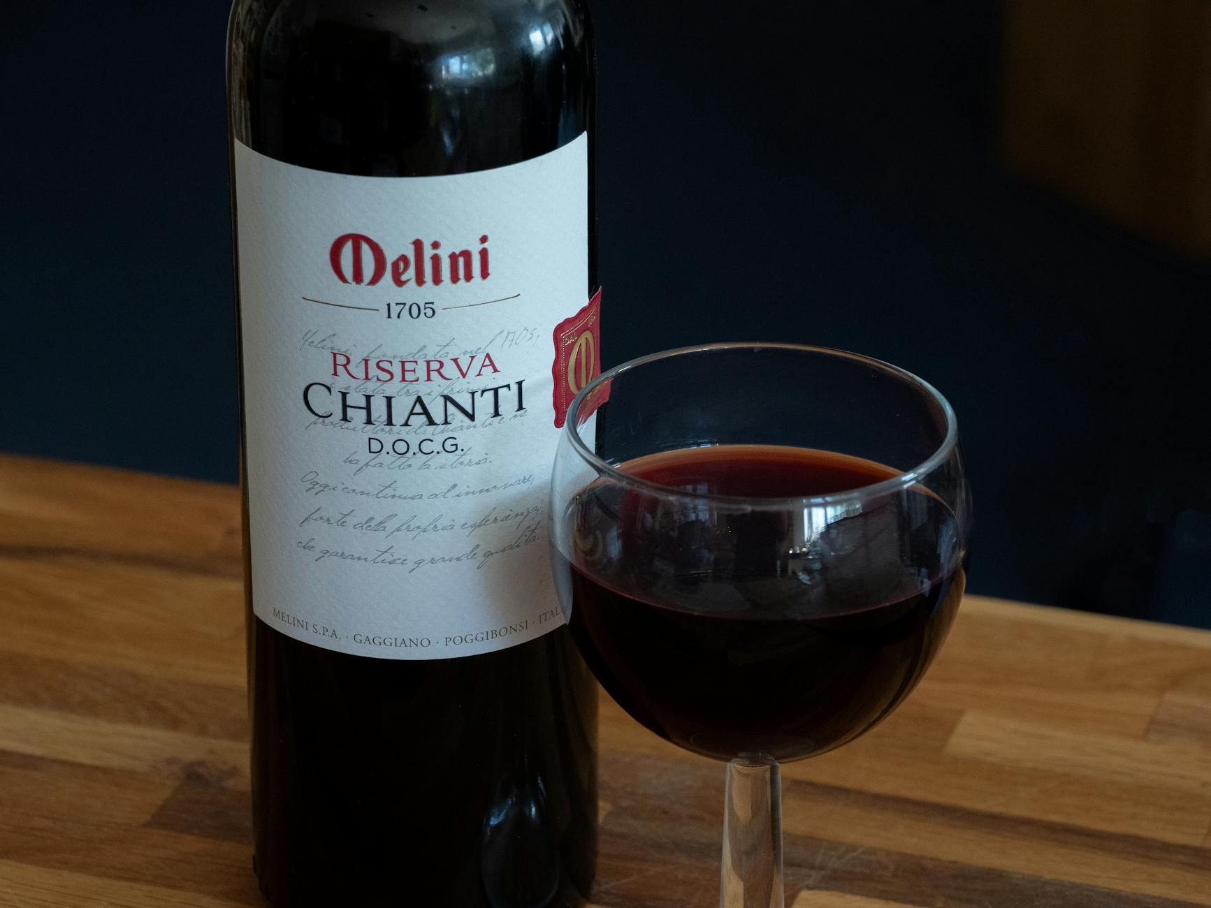 A bottle of Melini Riserva Chianti D.O.C.G. with a glass of red wine on a wooden table.