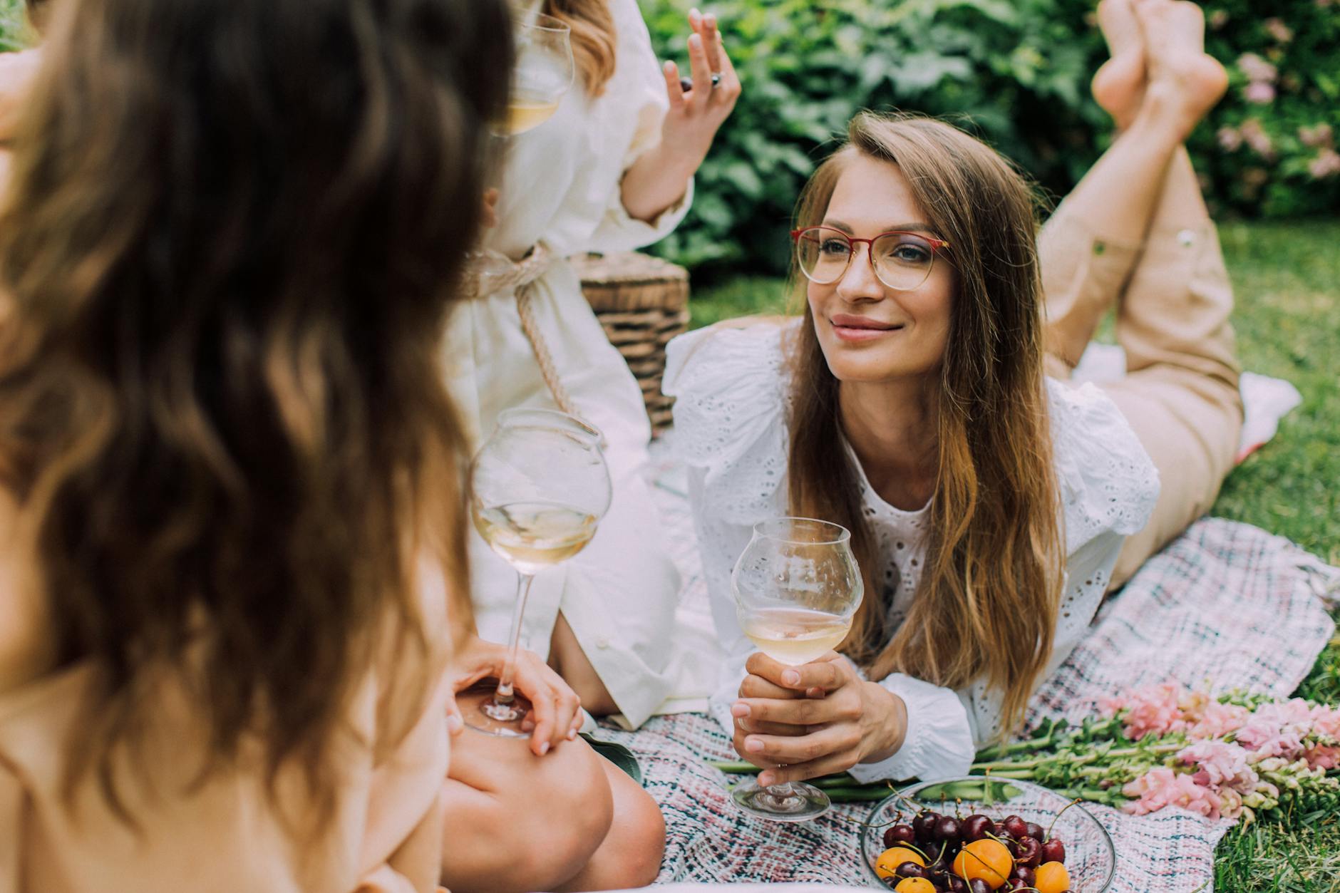 Enjoy a serene summer picnic with friends, featuring wine and fresh fruits on a lush green lawn.