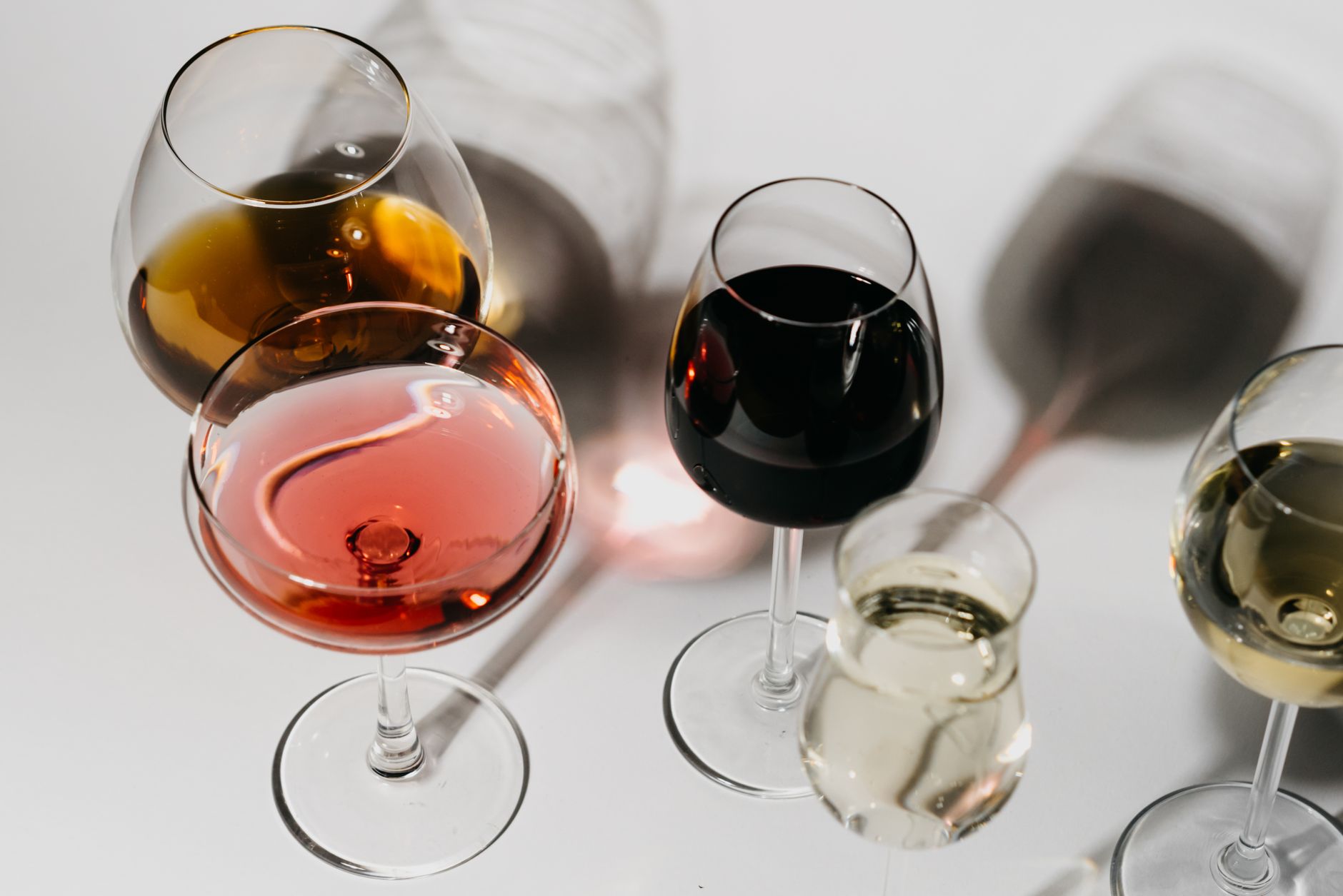 A variety of wine glasses on a clean white surface, showcasing different types and colors of wine.