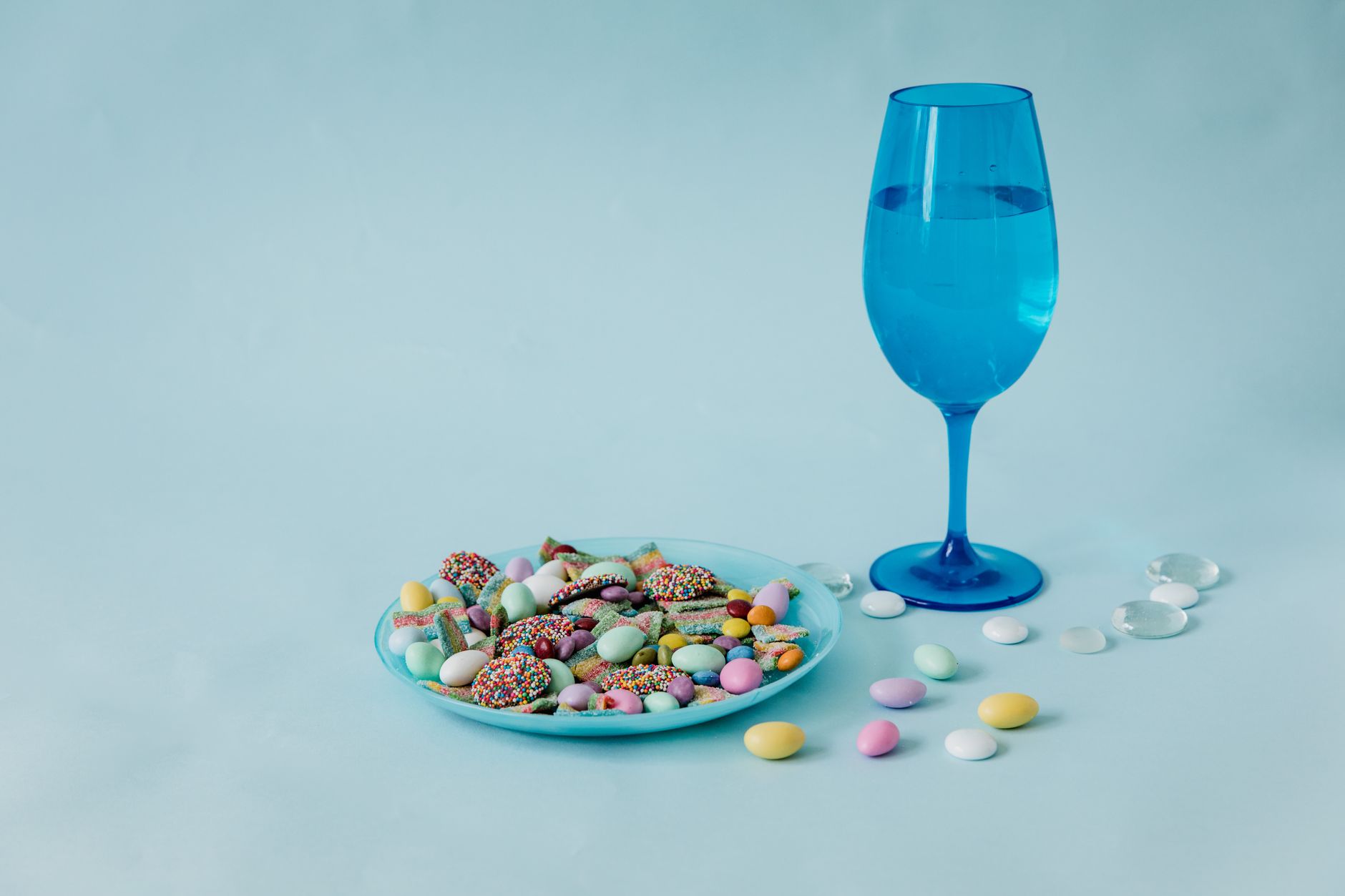 Colorful candies and a blue glass on pastel background, shot in studio.